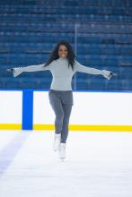 A skater in a t-pose smiling in an ice rink