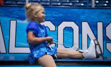 A child sits and ties skates while looking off toward to right and smiling.